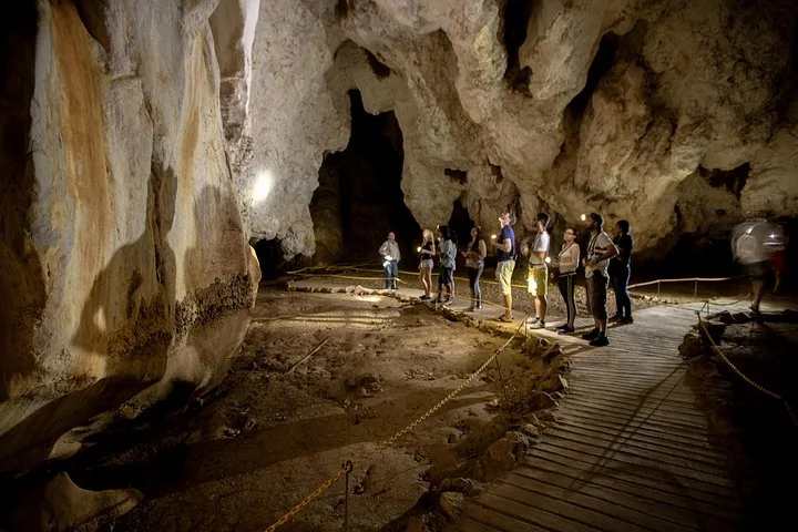 Eine Gruppe von Touristen erkundet mit Stirnlampen das Innere einer großen Höhle.