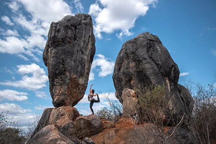Eine Frau macht eine Yoga-Pose auf einer Felsformation vor blauem Himmel.