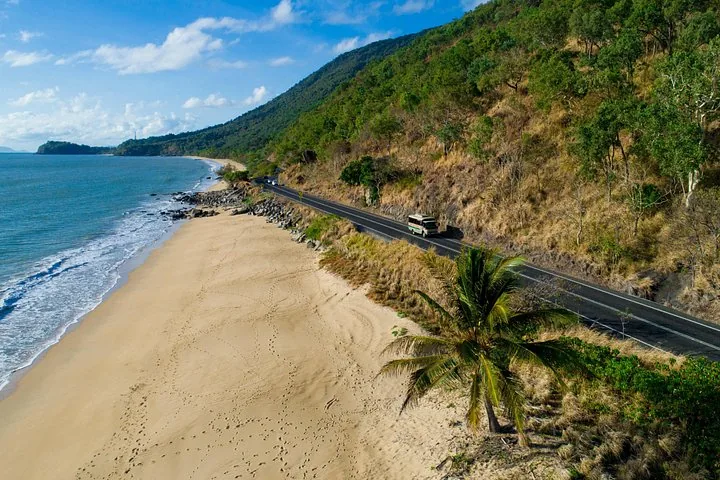 Ein Tourbus fährt auf einer Küstenstraße neben einem Sandstrand.