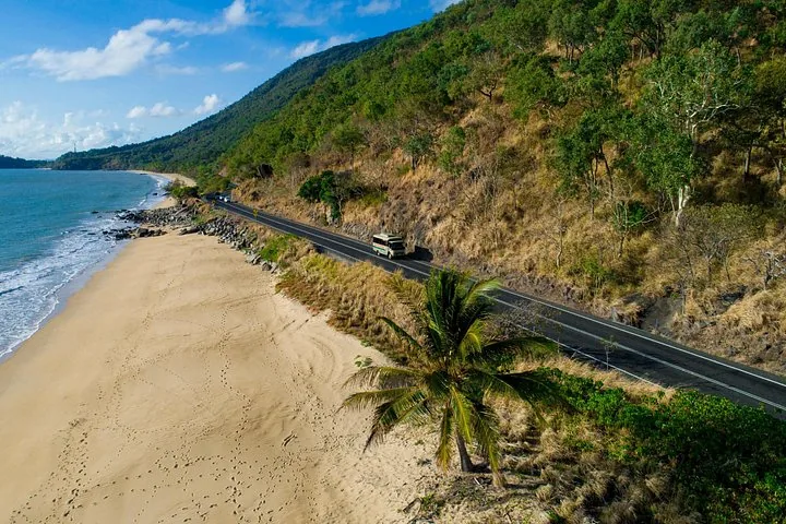 Ein Tourbus fährt auf einer Küstenstraße neben einem Sandstrand.